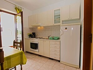 Una cocina con armarios blancos, estufa, horno, refrigerador y una mesa de comedor con mantel verde.