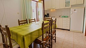 Een eetgedeelte met een tafel gedekt voor vier personen, een keuken met witte kasten, een koelkast en een raam met gordijnen.