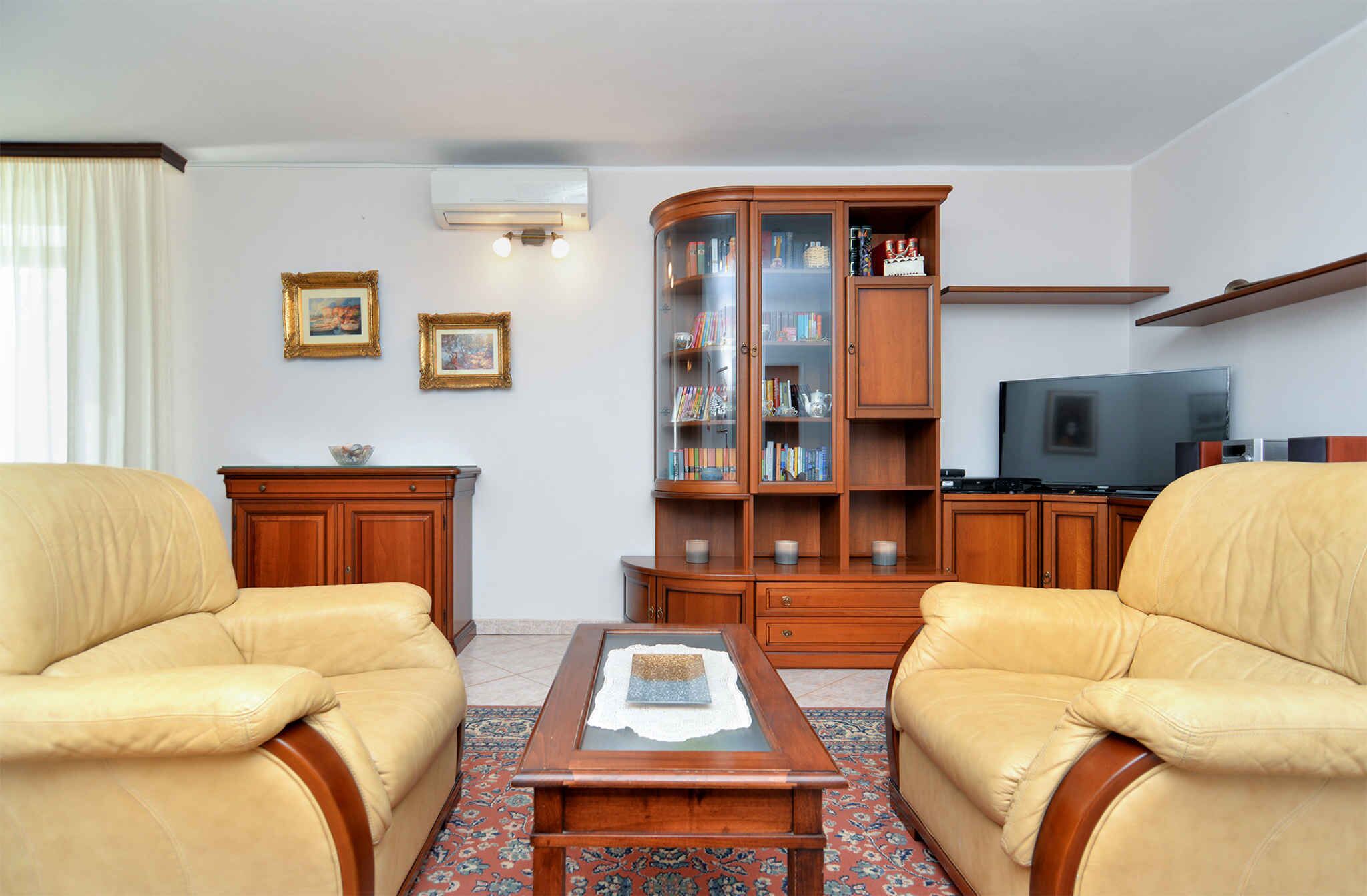 A living room with two leather armchairs, a wooden cabinet with glass doors, a television, and a small table with a book.