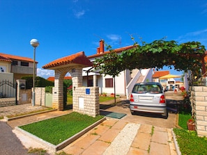 A residential area with a paved driveway, a car parked in front of a house, and a stone archway.