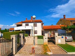 A two-story house with a red-tiled roof, a satellite dish, and a gated entrance.