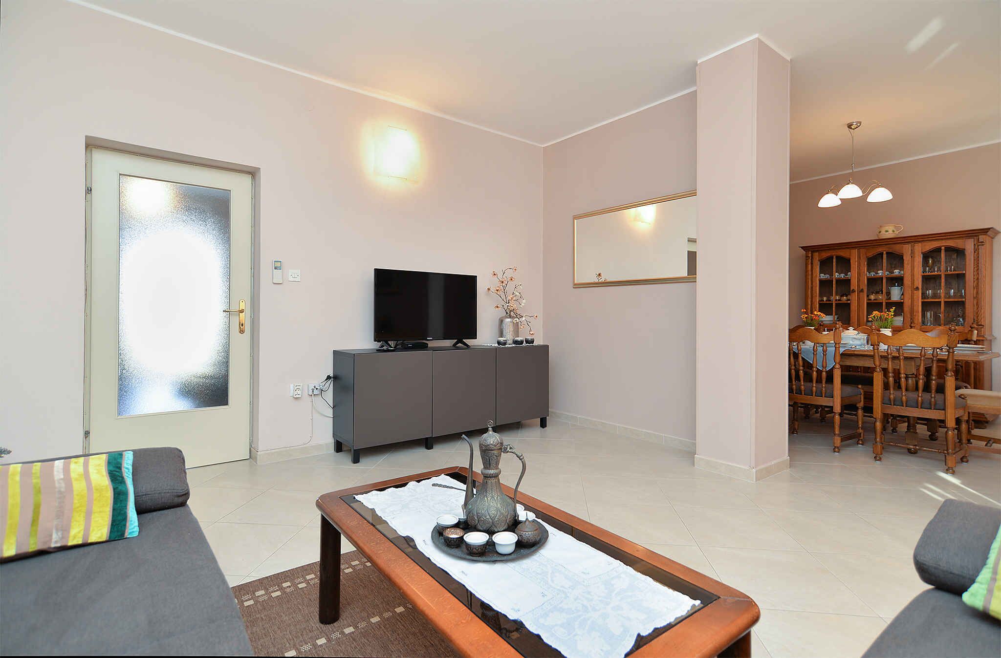 A living room with a sofa, a coffee table with a decorative item, a television on a cabinet, and a dining area with a table and chairs.