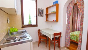 A compact kitchen with a sink, stove, and a small dining table with chairs. There is a window with a view of greenery outside. - Holiday apartment with terrace (Štinjan)