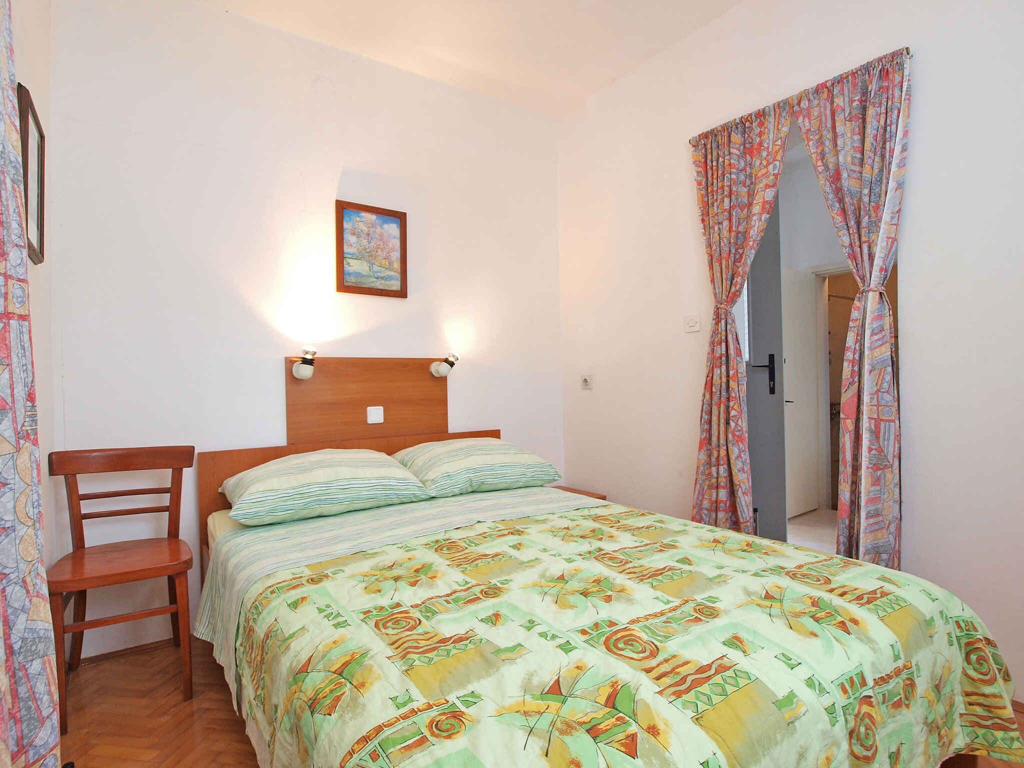 A bedroom with a wooden bed, a chair, a painting on the wall, and patterned curtains.