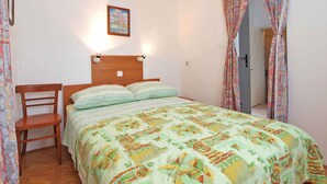 A bedroom with a wooden bed, a chair, a painting on the wall, and patterned curtains. - Holiday apartment with terrace (Štinjan)