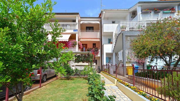 Un edificio residencial con balcones, un jardín con flores y un coche estacionado.