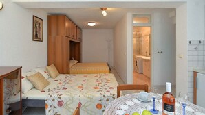 Habitación pequeña con una cama, una mesita con una taza y copas de vino, y un área de ducha visible a través de una puerta abierta.