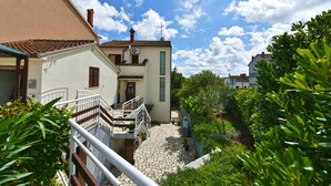 A courtyard with a stone pathway, a white building with a red-tiled roof, and lush greenery. - Holiday flat with air conditioning and barbecue facilities (Pula)