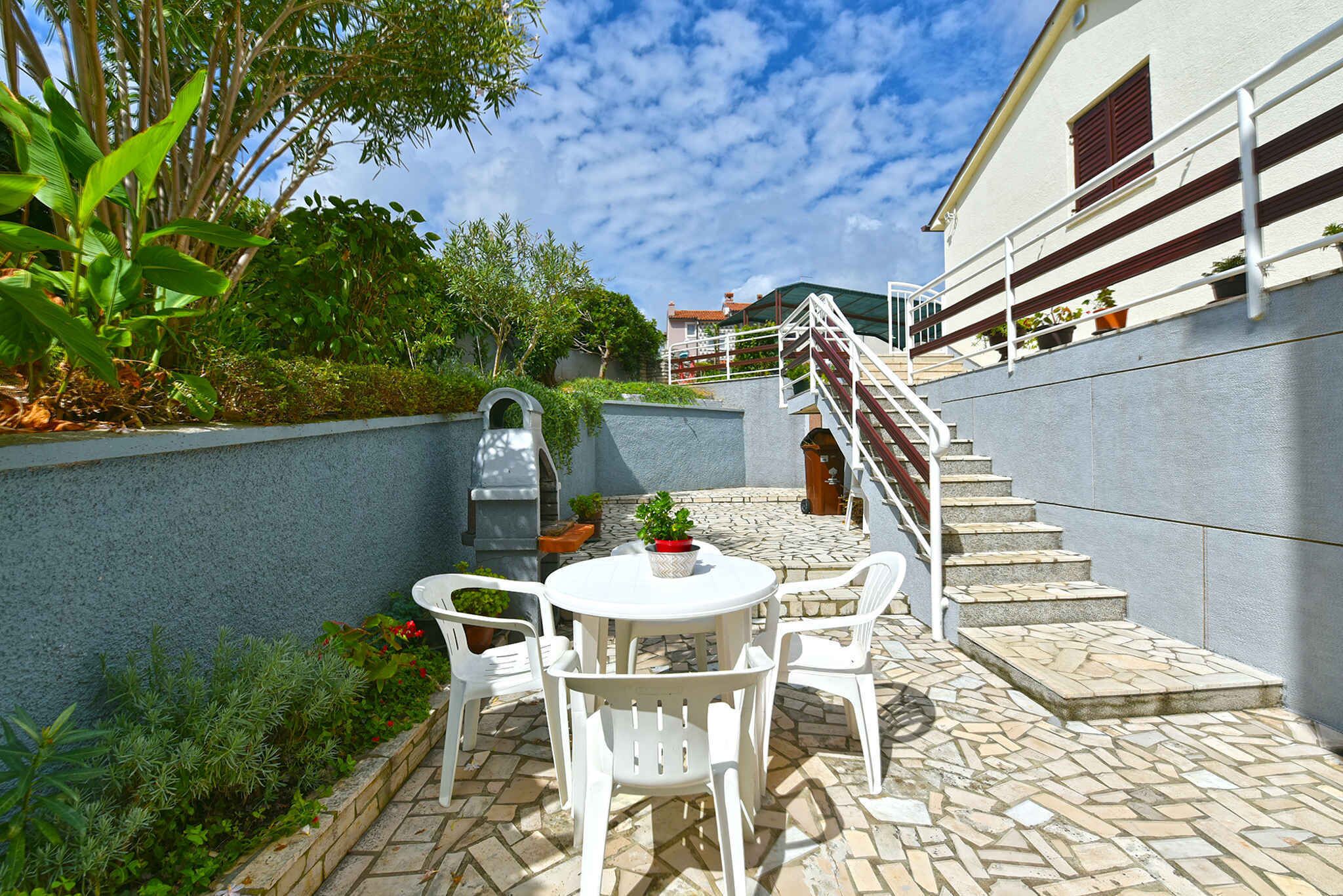 A patio with a white table and chairs, surrounded by greenery and a stone wall.