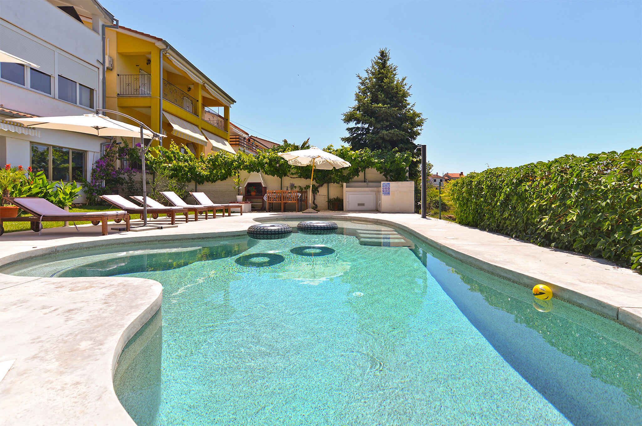 Una piscina amb gandules i ombrel·les, envoltada per un edifici amb balcons i un bord.