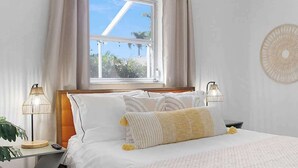 A neatly made bed with white bedding and striped pillows, a bedside lamp, and a wall decor piece. - Free Early Check-in / Min to Beaches/ Heated pool (Bradenton)