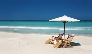 Een strand met twee houten ligstoelen en een witte parasol.