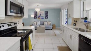 A modern kitchen with white cabinets, a built-in microwave, and a stove. There is a grey sofa in the living area with a chandelier above. - Free Early Check-in / Min to Beaches/ Heated pool (Bradenton)