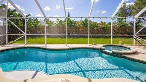 A swimming pool with a glass enclosure, surrounded by a grassy yard and a wooden fence. - Free Early Check-in / Min to Beaches/ Heated pool (Bradenton)