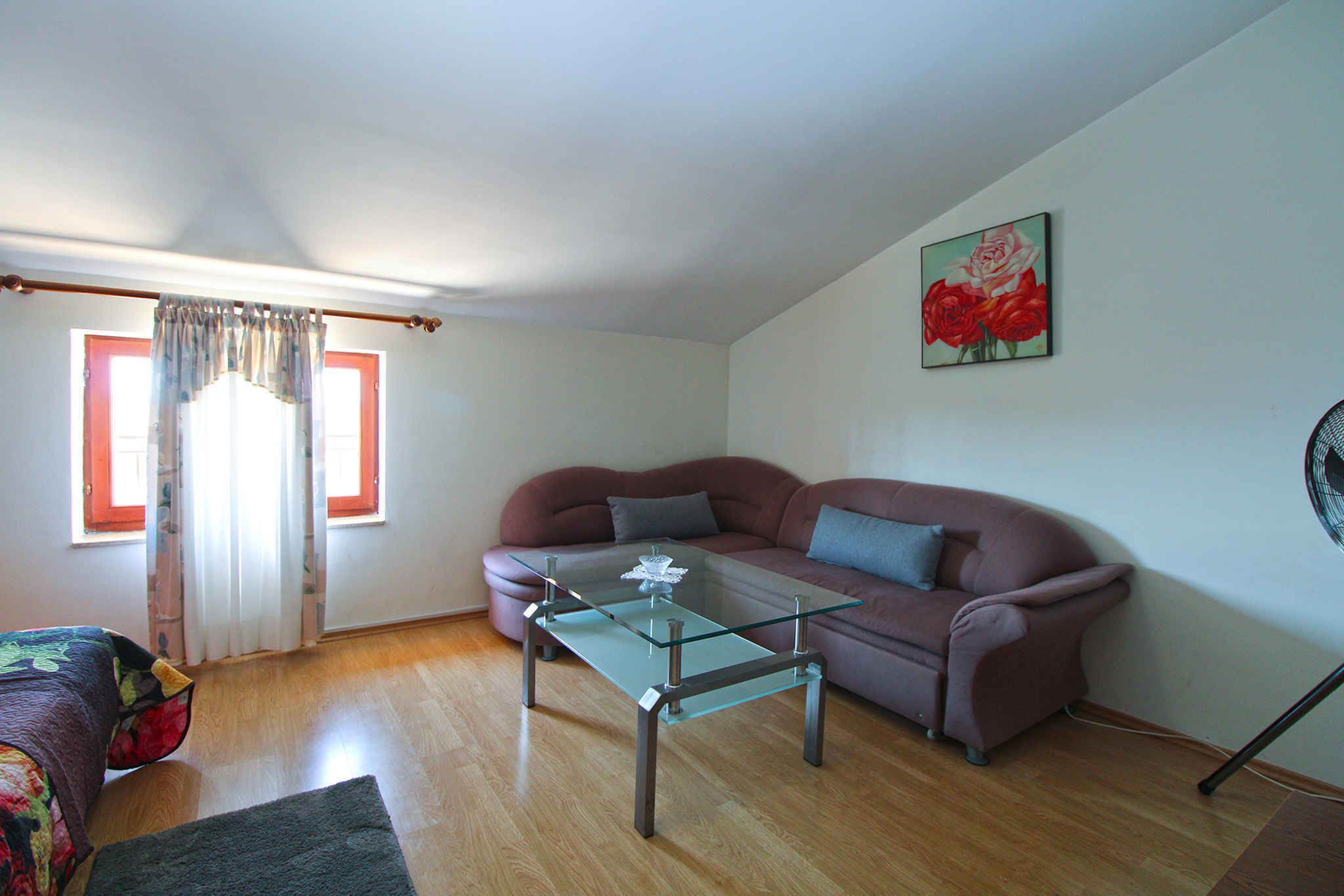 A living room with a glass coffee table, a red sofa, and a painting of roses on the wall.