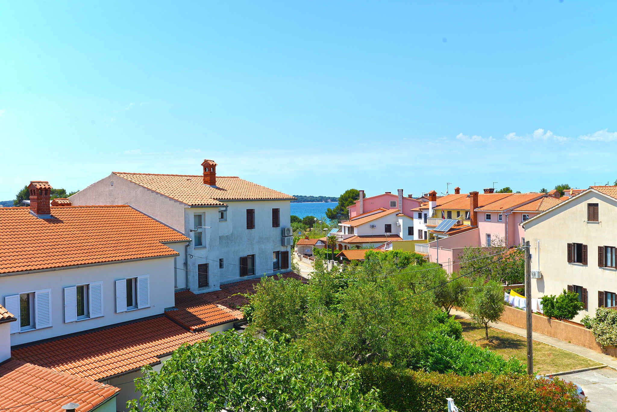 A coastal residential area with terracotta-tiled roofs, white and pastel-colored buildings, and lush greenery.