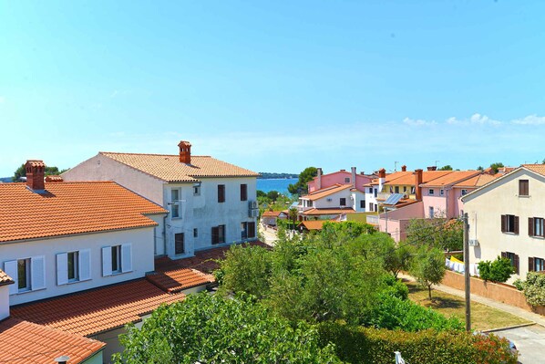 A coastal residential area with terracotta-tiled roofs, white and pastel-colored buildings, and lush greenery.