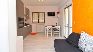 En kompakt bolig med tekøkken, spiseplads og en sofa med en pude formet som en avis.