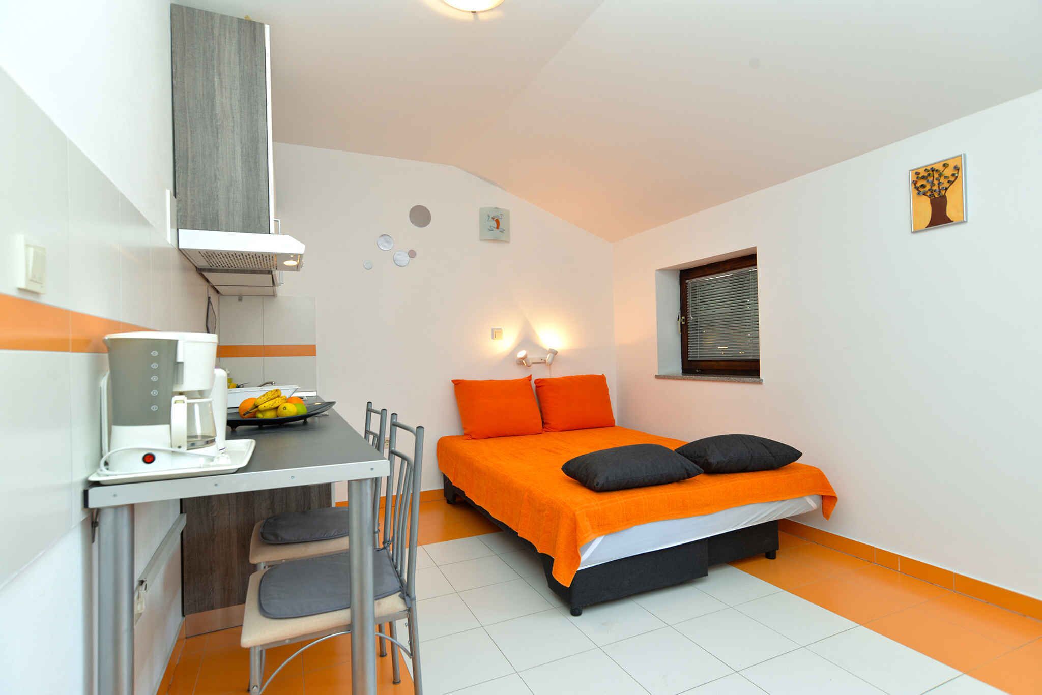 A compact room with a bed, a desk with a chair, a coffee maker, and a fruit bowl.