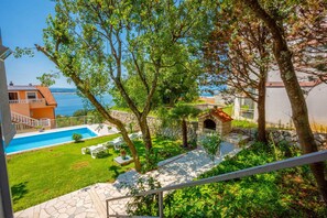 A pool area with a stone pathway, outdoor seating, and a view of the sea. - Holiday apartment with shared pool (Dramalj)
