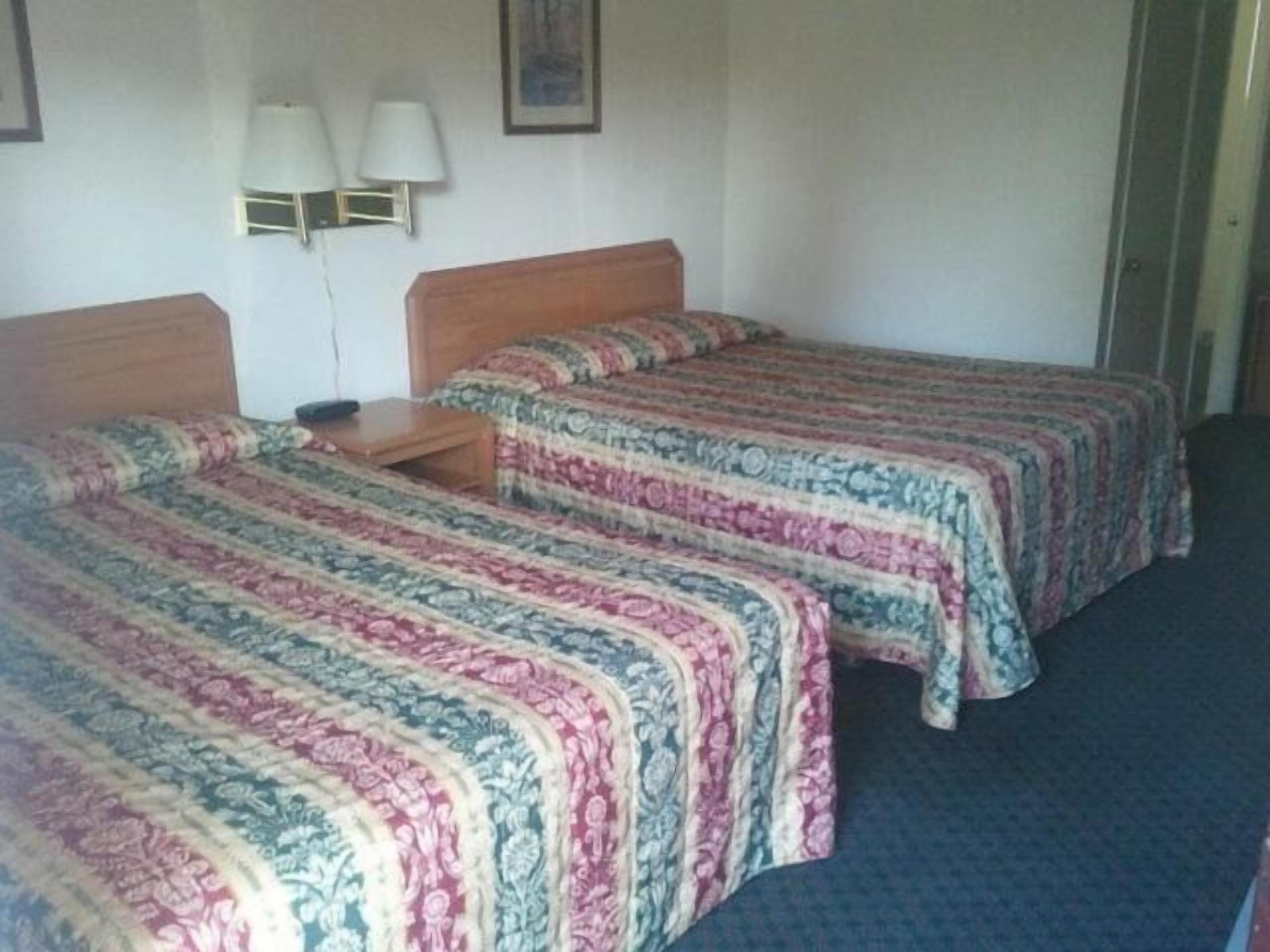 Habitación de hotel con dos camas individuales, cada una con colcha estampada, una mesita de noche y una lámpara de pared.