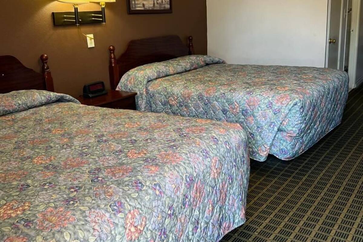 A hotel room with two beds, a nightstand, a lamp, and a framed picture on the wall.
