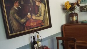 Comedor con mantel rojo, dos sillas, un cuadro, un jarrón con flores y un botellero con botellas de vino.