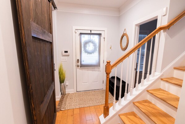 Un escalier avec des marches en bois et une rampe blanche, menant à une porte ornée d’une guirlande.