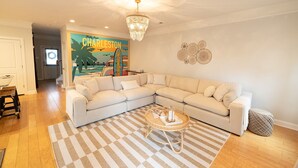 A living room with a large L-shaped beige sofa, a checkered rug, a round coffee table, and a chandelier. - The Palmetto @ Park Circle - 10 Minutes From Downtown, The Palmetto @ Park Circle (North Charleston)
