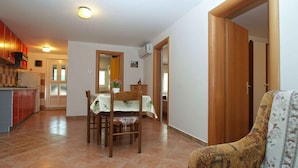A spacious living area with a dining table, chairs, and a sofa. There is a kitchen area with cabinets and a refrigerator.