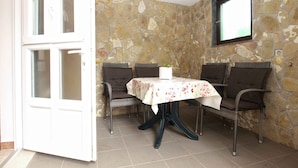 A room with a stone wall, a table with a floral tablecloth, and wicker chairs.