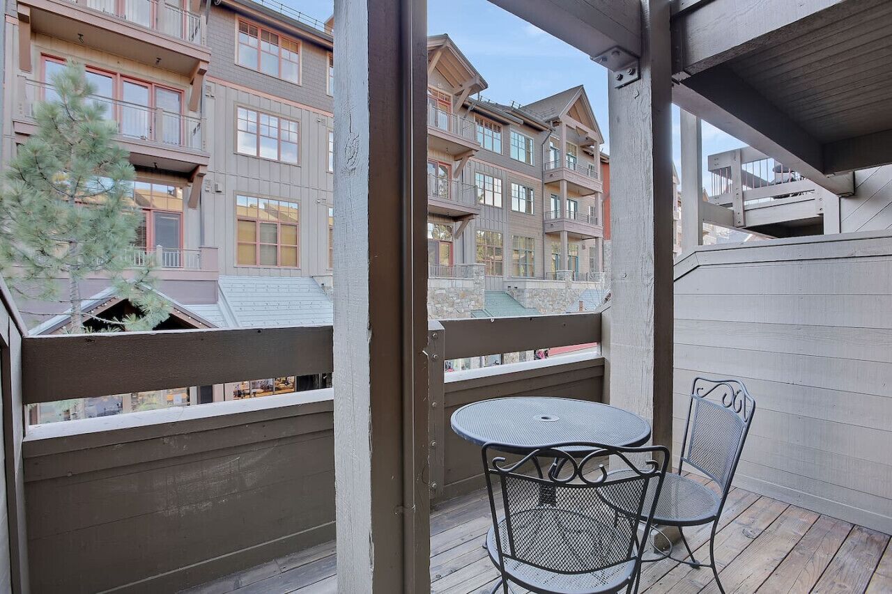 A balcony with a metal table and chairs, overlooking a row of multi-story buildings.