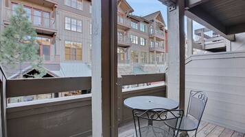 A balcony with a metal table and chairs, overlooking a row of multi-story buildings.