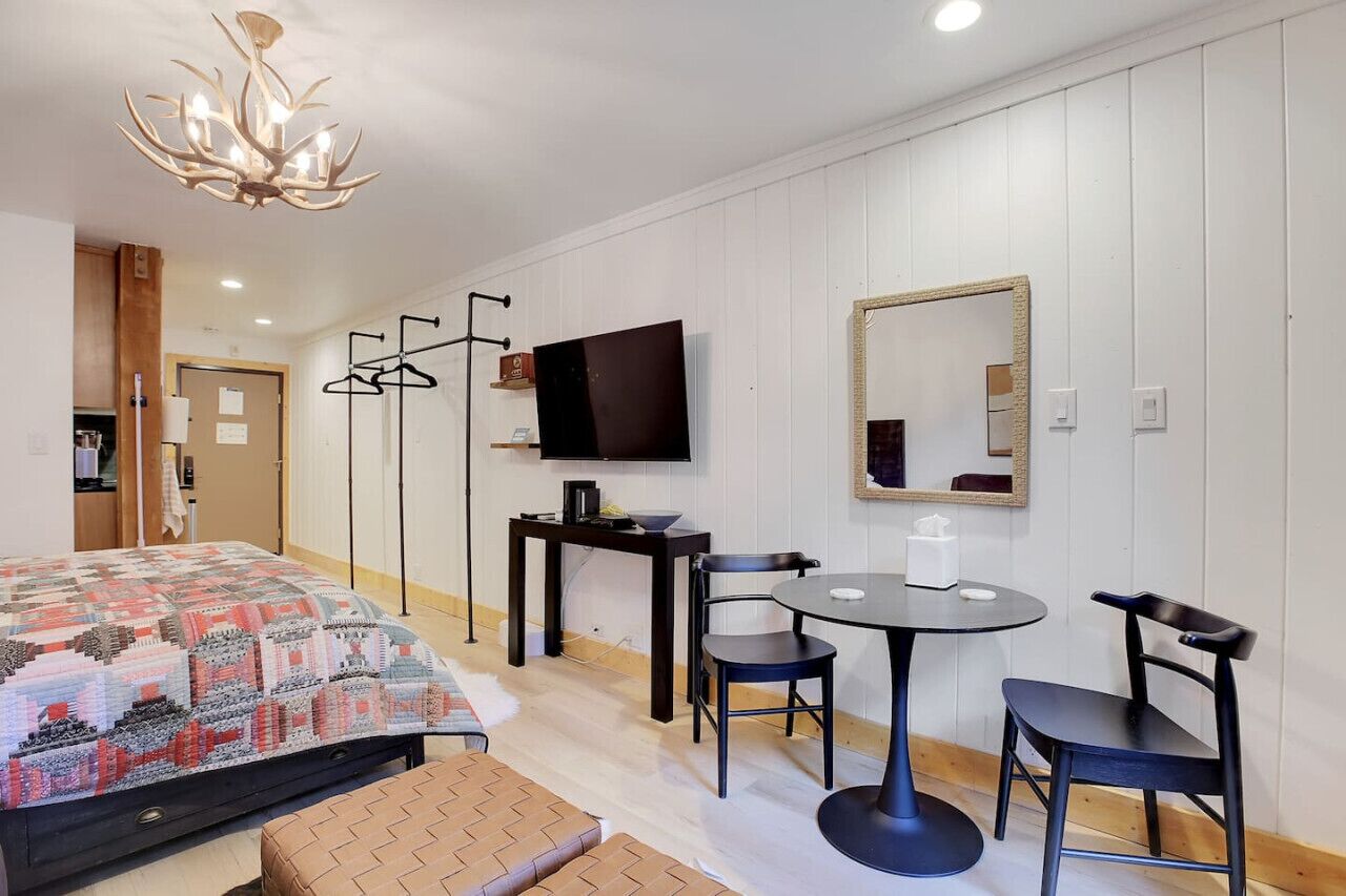 Habitación de hotel con cama, televisión, mesa y sillas, espejo y candelabro.