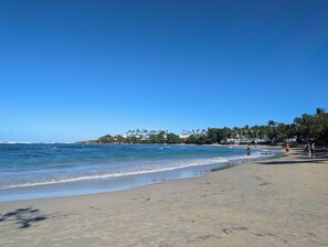 Une plage avec un ciel dégagé, une eau calme et quelques personnes qui se promènent.