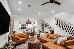 A modern living room with brown leather sofas, a dining area, and a kitchen in the background. - Home away from home Downtown comfort Skyline View Minutes walk to Metro rail (Houston)