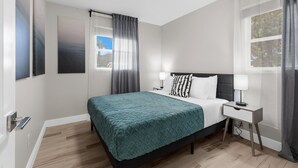 Un dormitorio moderno con cama, mesitas de noche y vistas al exterior.
