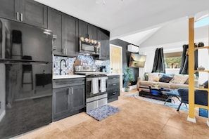 Une cuisine moderne avec des meubles de couleur sombre, un four à micro-ondes et une cuisinière. On y trouve également un espace salon avec un canapé et une table basse.