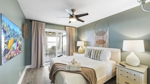 Une chambre d’hôtel avec un lit, des tables de chevet, un ventilateur de plafond et une grande fenêtre avec des rideaux.