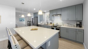 Une cuisine moderne dotée d’un grand îlot central, de meubles gris, d’appareils électroménagers en acier inoxydable et de luminaires suspendus.
