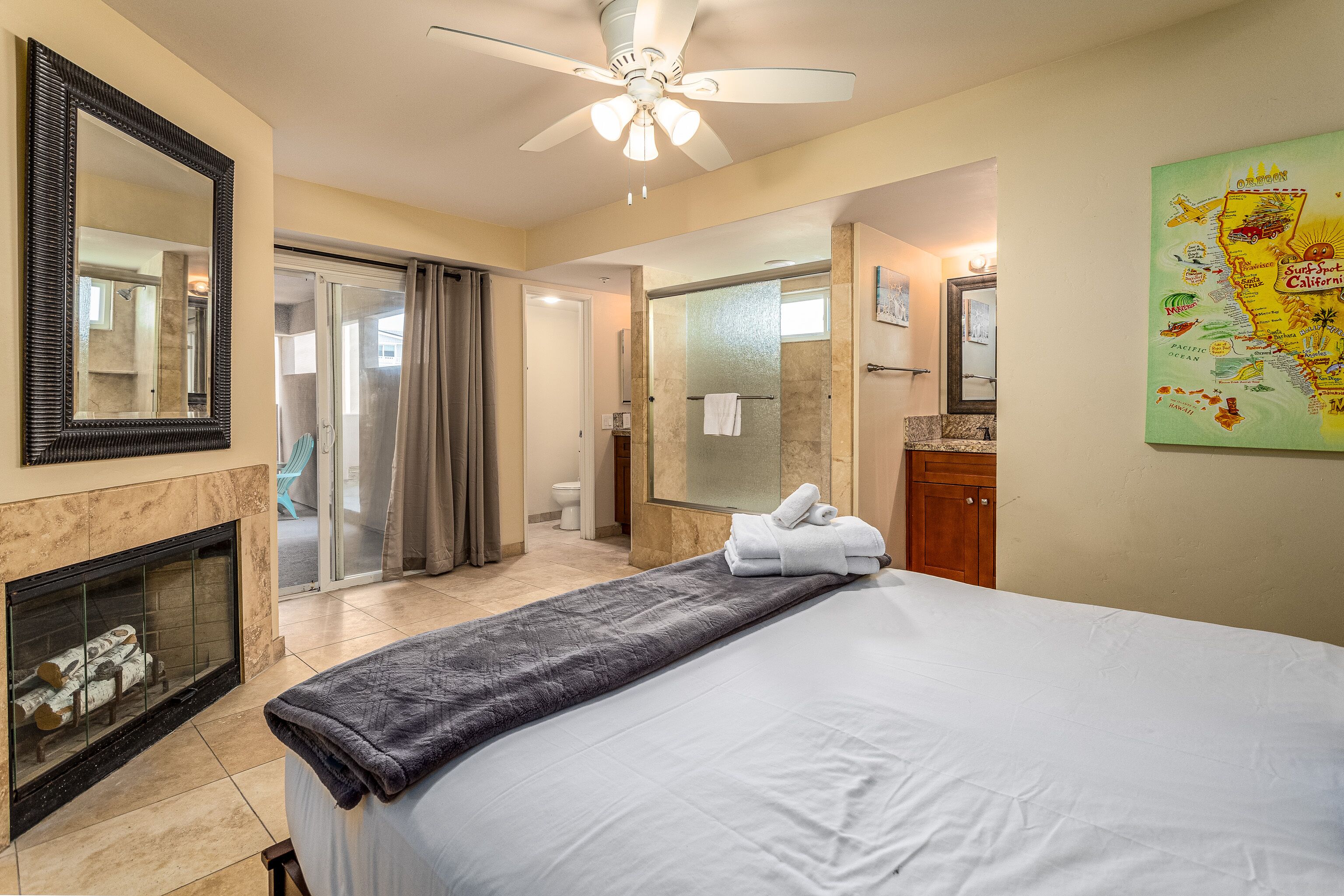 A hotel room with a bed, a fireplace, a ceiling fan, a bathroom with a shower, and a map on the wall.