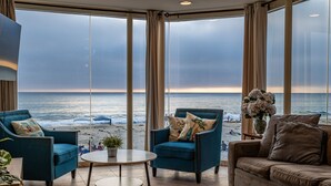 A room with a large window overlooking the beach, two armchairs, a sofa, and a small table.