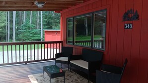 Un porche couvert avec un mur rouge, deux chaises noires, une petite table et une grande fenêtre.