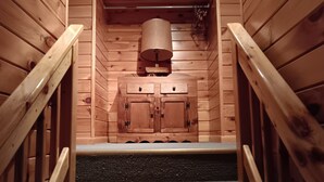 Un escalier en bois avec une rampe en métal, menant à une pièce où se trouve un meuble en bois et un objet cylindrique suspendu au plafond.