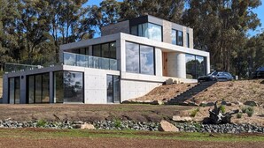 A modern two-story house with large glass windows, a flat roof, and a stone base. - Unveil a masterpiece in architectural design!  (Hepburn)