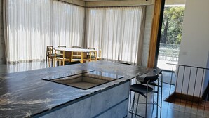A modern kitchen with a central island, a dining area with chairs, and large windows with curtains. - Unveil a masterpiece in architectural design!  (Hepburn)
