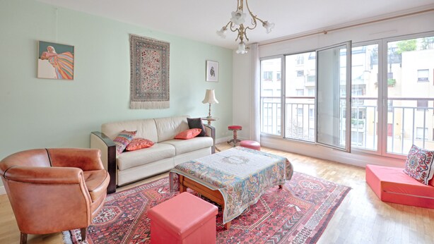 A spacious living room with a large window, a sofa, a chair, and a coffee table. - Appartement Martino - Welkeys (Paris)