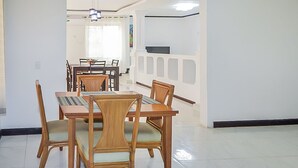 Zona pranzo con tavolo e sedie in legno, ventilatore a soffitto e interni bianchi.