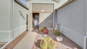 A narrow courtyard with a white wall, a garage door, and a small door leading to a garage. There are several cacti and decorative pots on the ground. - Green Valley Getaway Near Golfing: Pool Access! (Green Valley)