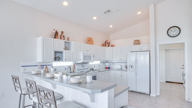 A modern kitchen with white cabinets, a central island with bar stools, and various kitchen appliances. - Green Valley Getaway Near Golfing: Pool Access! (Green Valley)